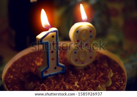 burning candles on a cake in the form of the number eighteen, coming of age, blurred image
