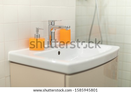 White bathroom sink white orange soap container - brown furniture and white faience. Clean picture