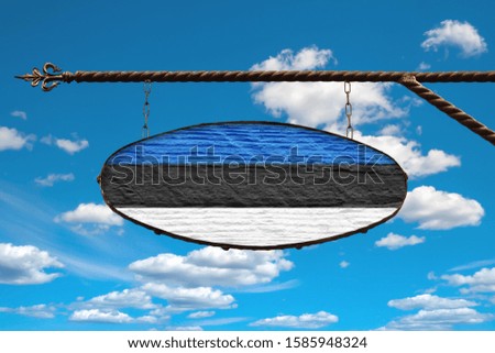 Estonia flag on a signboard. Oval signboard colors Estonia flag hanging on a metal forged structure. Template on a background of blue sky with clouds. Blank for creativity and design.