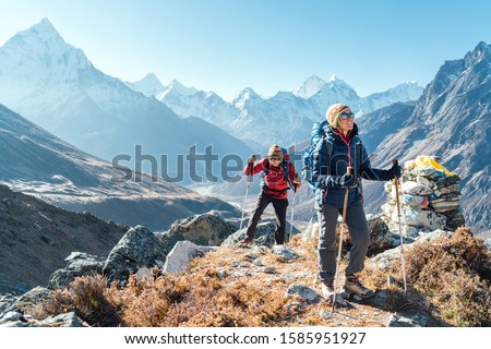 Couple following Everest Base Camp trekking route near Dughla 4620m. Backpackers carrying Backpacks and using trekking poles and enjoying valley view with Ama Dablam 6812m peak Royalty-Free Stock Photo #1585951927