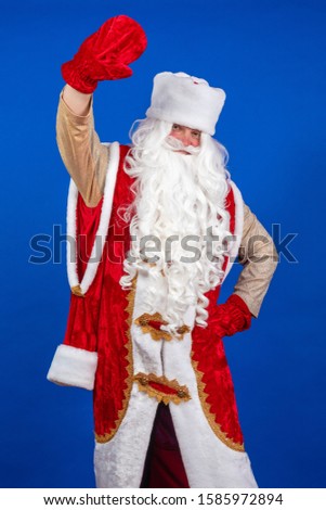 Emotional Santa Claus with a long white beard in a red coat and white hat posing on a blue background