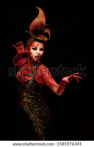 Young woman dancing in the image of Flames and Fire in a red body art emotionally posing on a black background