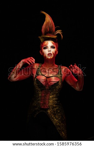Young woman dancing in the image of Flames and Fire in a red body art emotionally posing on a black background