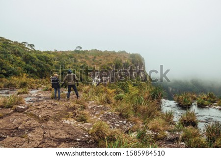 People on edge of cliff and mist coming up from the green valley at Serra Geral National Park near Cambara do Sul. A small rural town in southern Brazil with amazing natural tourist attractions.