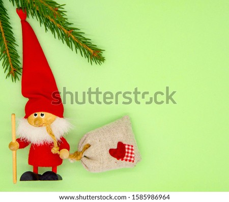 Fir branches and Christmas tree toy Santa Claus with a bag of gifts on a delicate green background. Copy space, top view, flat lay