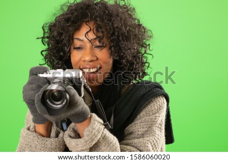 African female in winter clothes checking photos on camera on green screen. Happy woman looking through pictures