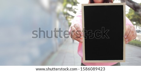 Woman with hand holding showing black chalkboard close up on outdoor blurred background, frame composition with copy space for banner design or card and online shopping marketing or school project