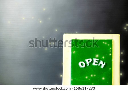 Close up of a green with yellow "OPEN" chalkboard sign leaning against sparkle ,bright with black background.