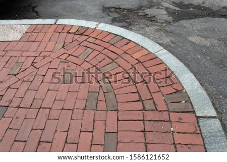Old brick sidewalk bordered with granite alongside crumbling asphalt street, horizontal aspect