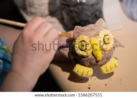 Female artist is using a painting brush on fairytale brown and yellow owl