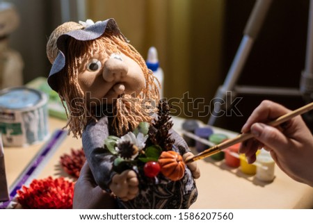 Female artist is using a painting brush on fairytale character Domovoy that looks like an old man from medieval