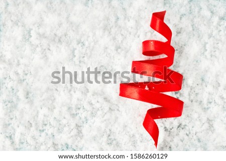 Silk red ribbon twisted in the form of a Christmas tree in the snow. Background for greeting card, poster, banner or invitation for the new year 2020 with copy space.