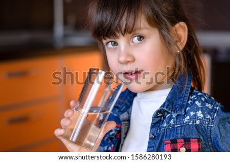 Adorable smiling little girl drinking water in kitchen. Health and beauty concept