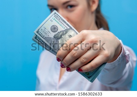 Unidentified young beautiful blurred woman holding dollar bills in her hands posing on a blue background. Cashback and stock concept. Advertising space