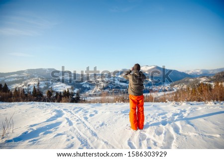 Hiker taking pictures of winter mountain landscape on phone. Snow-capped Carpathian Mountains. Place for text.