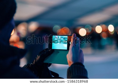 male hands holding a mobile phone on photo camera mode - man taking picture of a ice skating rink by night