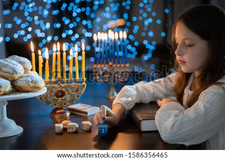 Child girl Looking at Menorah Candles on wooden table and sufganiyot on background light glitter bokeh overlay. Hanukkah jewish holiday Israel hebrew traditional family celebration invitation design
