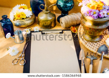 Vintage composition. Closeup clip board with scissors and vintage garden tools with flowers around on wooden background.