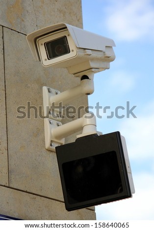Security camera with a screen below on an outdoor wall