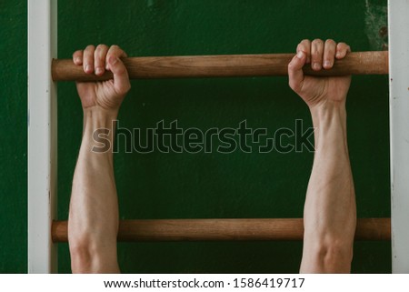 Gymnast's hands hold tightly on the horizontal bar of the Swedish wall in the gym close-up
