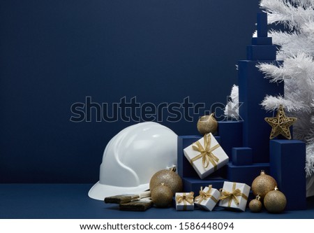 Construction hard hat, white fir tree, gift boxes and Christmas ornaments on dark blue background with copy space. New Year and Christmas construction background. For advertising or web design