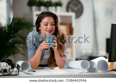 Young casual woman drinking coffee in office.
Attractive female manager sitting at desk after hard working day
