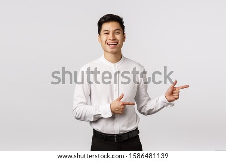 Carefree charismatic asian young 25s man in formal outfit, white shirt, black pants, invite check out and see event banner, pointing right and smiling, laughing amused, standing white background