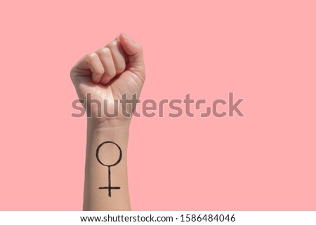 A woman hand and feminist sign tattoos on her hand isolate on pink background 