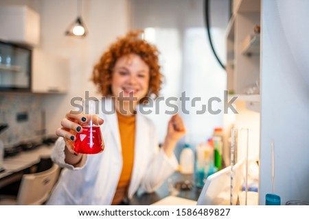 A female medical or scientific researcher or woman doctor looking at a test tube of clear solution in a laboratory with her microscope beside her. Young female geneticists looking in sample