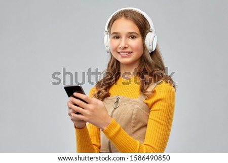 audio equipment and technology people concept - smiling teenage girl in headphones listening to music on smartphone over grey background