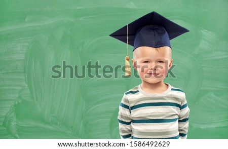 elementary school, preschool education and childhood concept - portrait of smiling little boy in mortar board over green chalk board background