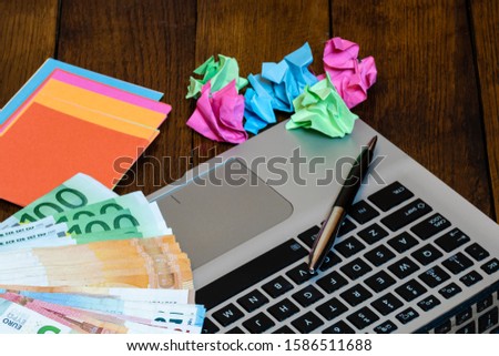 Different objects on wooden office desk. Modern wooden office desk table with laptop keyboard, pen, blank colorful sticky notes, money and crumpled paper.