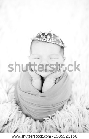 cute newborn sleeping baby picture like newborn potato in wrap. Portrait of newborn baby girl wrapped in wrap with crown headband 