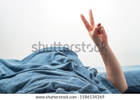 Female hand in bed shows victory gesture on a white background close up.
