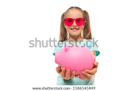 Fashionable teenager girl in blue t-shirt holds a pink pig moneybox and smiles, portrait isolated on white background