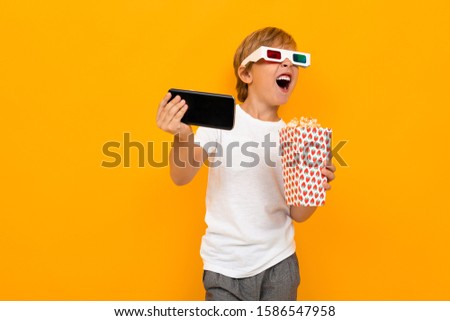 admiring boy in glasses for a movie theater with popcorn and a telephone on a yellow background
