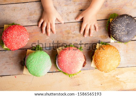 A kid holding hands near colorful small burgers on wooden table, hands in the picture, top view