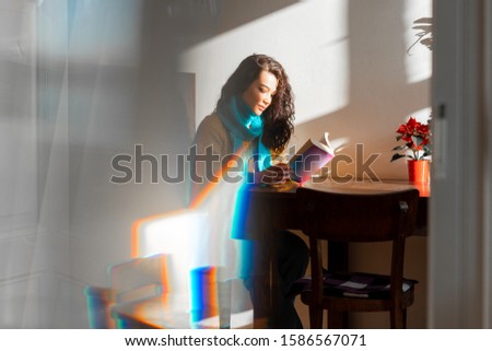Beautiful Woman in Yellow Sweater And Blue Scarf Reading a Book In Modern Cafe. Concept of Slow Lifestyle. Photo With Light Through the Prism. Image With Noise and Grains