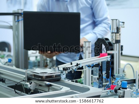 Focus on automated car which is on smart factory production line and programming engineer at the background. Industry 4.0 workshop in an automation education center. Engineer is programming PLC. Royalty-Free Stock Photo #1586617762