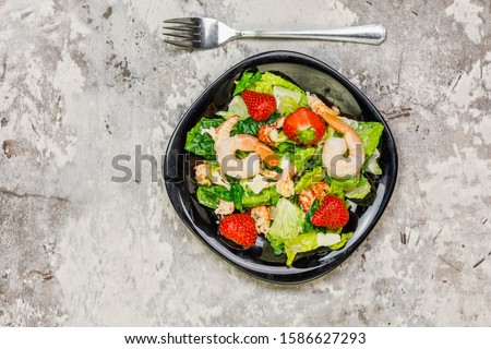 Caesar salad with shrimps on black backgound, top view