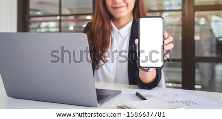 Mockup image of an asian businesswoman holding and showing black mobile phone with blank white screen in cafe