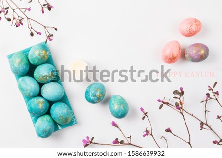 Happy easter card. Stylish minimalistic composition of turquoise with gold easter eggs on a white background. Candles and delicate spring flowers. Flat lay, top view, copy space.