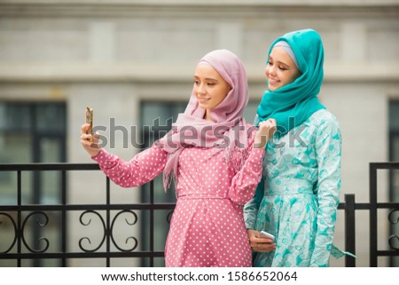 two beautiful young women in muslim dresses are photographed on the phone