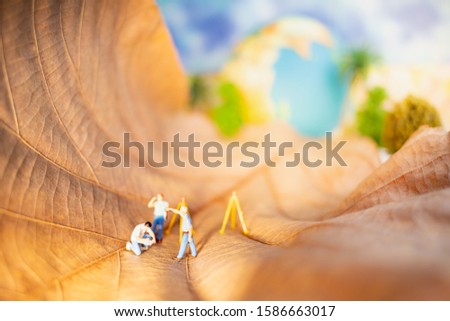 Miniature people: Worker working on brown leaf with world globe using as background thinking and saving, happy  earth day, world environment day, save the earth concept.