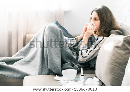 concept of a person suffering from a cold. different items needed for colds - spray and handkerchiefs, a cup of tea and pills, in the background a girl in pajamas blows her nose in a scarf Royalty-Free Stock Photo #1586670010