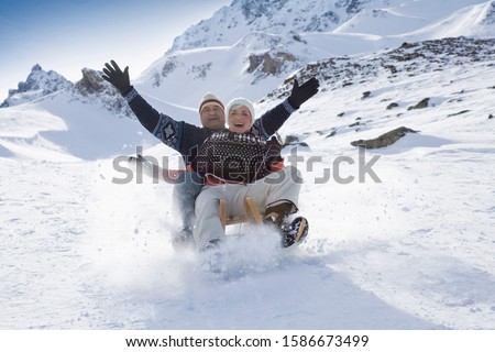 Senior couple sledding in mountains on winter day