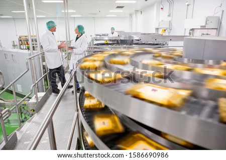 Quality control workers talking behind production line in cheese processing plant