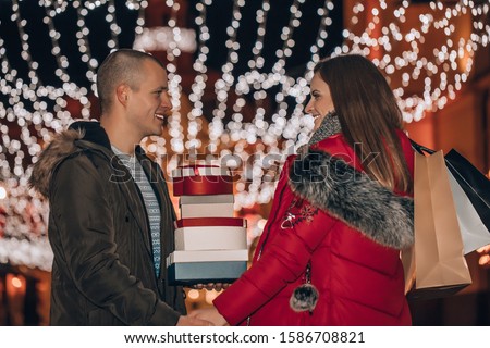 Young cheerful couple is having fun in the city street at the Christmas night. Young man and woman are laughing, walking and buying presents for their darlings and each other.

