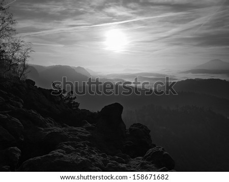 Sunrise in a beautiful mountain of Bohemian-Saxony Switzerland. Sandstone peaks and hills increased from foggy background. First sun rays. Black and White photo.