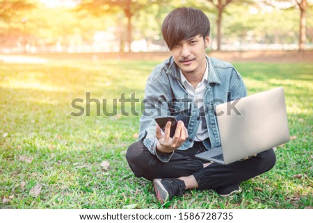 A young man with a laptop sitting on the lawn.